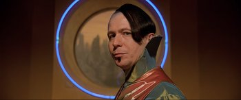 Movie still from “The Fifth Element” (1997), directed by Luc Besson – A man in a futuristic costume poses for a picture; Close Up shot, Over the shoulder angle