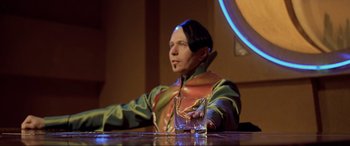 Movie still from “The Fifth Element” (1997), directed by Luc Besson – A man sitting at a table with a glass of water; Medium shot, Over the shoulder angle