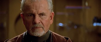 Movie still from “The Fifth Element” (1997), directed by Luc Besson – An older man with a gray beard wearing a brown jacket; Close Up shot, Over the shoulder angle