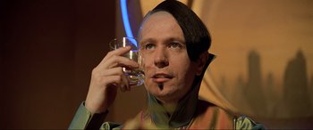 Movie still from “The Fifth Element” (1997), directed by Luc Besson – A man in a costume holding a glass of water; Close Up shot, Over the shoulder angle