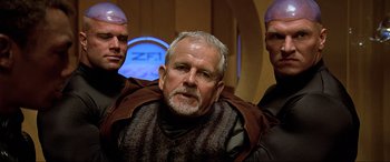 Movie still from “The Fifth Element” (1997), directed by Luc Besson – A man with a gray beard is surrounded by two other men; Close Up shot, Over the shoulder angle