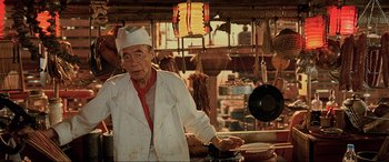 Movie still from “The Fifth Element” (1997), directed by Luc Besson – An old man wearing a chef's hat in a kitchen; Medium shot, Low angle