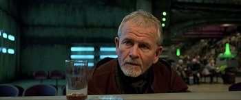Movie still from “The Fifth Element” (1997), directed by Luc Besson – An older man sitting in front of a glass of water; Close Up shot, Over the shoulder angle