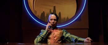 Movie still from “The Fifth Element” (1997), directed by Luc Besson – A man with a bald head talking on a cell phone in front of a city skyline; Medium shot, Low angle