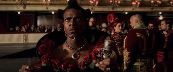 Movie still from “The Fifth Element” (1997), directed by Luc Besson – A man in a black and red dress holding a wine glass; Close Up shot, Low angle