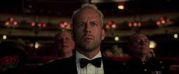 Movie still from “The Fifth Element” (1997), directed by Luc Besson – A man in a suit and bow tie in front of some people; Close Up shot, Low angle