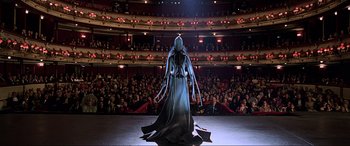 Movie still from “The Fifth Element” (1997), directed by Luc Besson – A woman in a black dress standing in front of an audience; Wide shot, Low angle