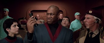 Movie still from “The Fifth Element” (1997), directed by Luc Besson – A man looking at his cell phone in front of a group of people; Close Up shot, Low angle