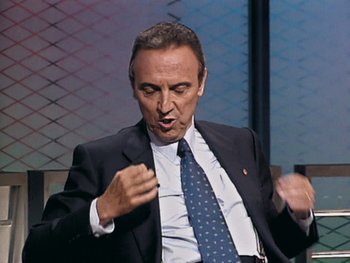 Movie still from “The Figo Affair: The Transfer that Changed Football” (2022), directed by Ben Nicholas – A person wearing a suit and tie; Medium shot, Low angle