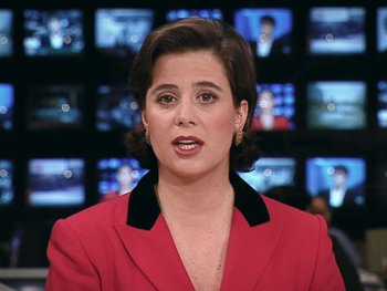 Movie still from “The Figo Affair: The Transfer that Changed Football” (2022), directed by Ben Nicholas – A woman wearing a red jacket is in front of a wall of tv screens; Close Up shot, High angle