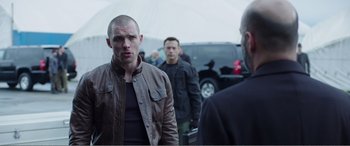 Movie still from “Deadpool” (2016), directed by Tim Miller – A group of men standing next to each other in a parking lot; Medium shot, Over the shoulder angle