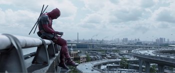 Movie still from “Deadpool” (2016), directed by Tim Miller – A man in a red suit sitting on the side of a building; Wide shot, Low angle