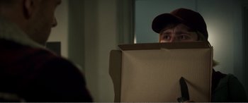 Movie still from “Deadpool” (2016), directed by Tim Miller – A person with a hat looking through a box; Close Up shot, Over the shoulder angle