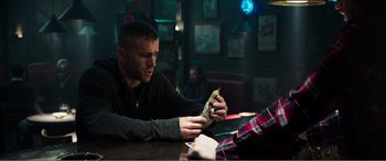 Movie still from “Deadpool” (2016), directed by Tim Miller – A man sitting at a table holding a piece of food; Medium shot, Over the shoulder angle