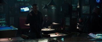 Movie still from “Deadpool” (2016), directed by Tim Miller – A man standing at a table in front of two other men; Wide shot, Over the shoulder angle