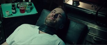 Movie still from “Deadpool” (2016), directed by Tim Miller – A man with a black collar laying in a chair; Close Up shot, Over the shoulder angle