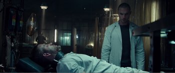 Movie still from “Deadpool” (2016), directed by Tim Miller – A man standing next to a man laying on a bed; Medium shot, Low angle