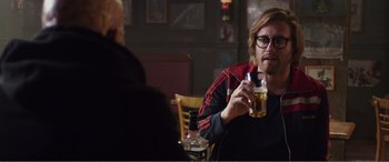 Movie still from “Deadpool” (2016), directed by Tim Miller – A man sitting at a table with a glass of beer in front of him; Medium shot, Over the shoulder angle