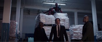 Movie still from “Deadpool” (2016), directed by Tim Miller – Two men in suits standing in front of a pile of papers; Wide shot, Low angle