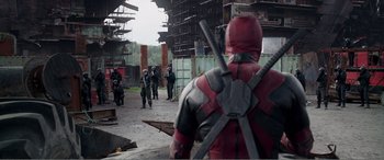 Movie still from “Deadpool” (2016), directed by Tim Miller – A group of people in a building with a person dressed as deadpool; Wide shot, Over the shoulder angle