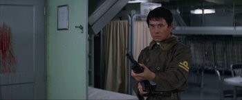 A man holding a gun while standing next to a bed