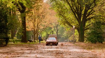 Movie still from “The Firm” (1993), directed by Sydney Pollack – A man walking down a road with a car parked in front of it; Extreme Wide shot, Low angle