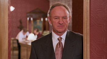 Movie still from “The Firm” (1993), directed by Sydney Pollack – A man in a suit and tie standing in front of a table; Close Up shot, Low angle