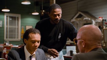 Movie still from “The Firm” (1993), directed by Sydney Pollack – A man standing next to another man at a table; Medium shot, Over the shoulder angle