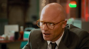 Movie still from “The Firm” (1993), directed by Sydney Pollack – A bald man wearing glasses and a suit and tie; Close Up shot, Over the shoulder angle