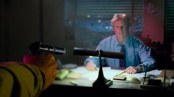Movie still from “The Firm” (1993), directed by Sydney Pollack – A man is sitting at a desk in front of a microphone; Medium shot, Over the shoulder angle