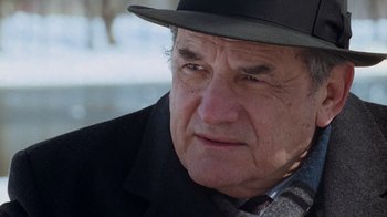 Movie still from “The Firm” (1993), directed by Sydney Pollack – An older man wearing a black hat and a black coat; Close Up shot, Over the shoulder angle