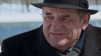 Movie still from “The Firm” (1993), directed by Sydney Pollack – An older man wearing a black hat and a black jacket; Close Up shot, Over the shoulder angle