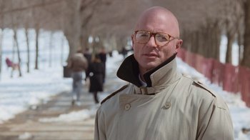 Movie still from “The Firm” (1993), directed by Sydney Pollack – A bald man wearing glasses and a trench coat; Close Up shot, Low angle