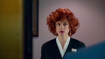 Movie still from “The Firm” (1993), directed by Sydney Pollack – A woman with red curly hair wearing a black suit; Close Up shot, Over the shoulder angle