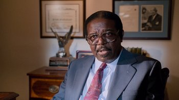 Movie still from “The Firm” (1993), directed by Sydney Pollack – A man in a suit and tie in front of a desk; Close Up shot, High angle