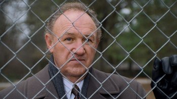 Movie still from “The Firm” (1993), directed by Sydney Pollack – An older man wearing a suit and tie behind a chain link fence; Close Up shot, Low angle