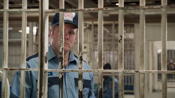 Movie still from “The Firm” (1993), directed by Sydney Pollack – A man standing behind bars in a jail cell; Medium shot, Over the shoulder angle