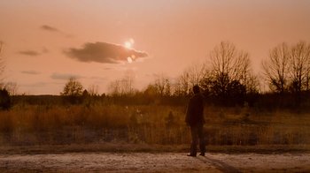 Movie still from “The Firm” (1993), directed by Sydney Pollack – A person standing on a dirt road near a field; Extreme Wide shot, Low angle