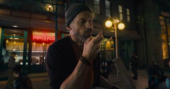 Movie still from “The Flash” (2023), directed by Andy Muschietti – A man with a beard is eating something outside at night; Close Up shot, Over the shoulder angle