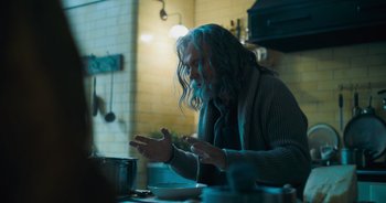 Movie still from “The Flash” (2023), directed by Andy Muschietti – A man sitting at a table with his hands raised; Medium shot, Over the shoulder angle