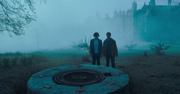 Movie still from “The Flash” (2023), directed by Andy Muschietti – Two people standing in front of a large metal object; Wide shot, High angle