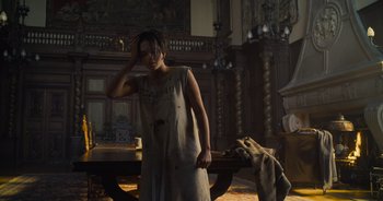 Movie still from “The Flash” (2023), directed by Andy Muschietti – A woman standing in a living room with her hand up to her head; Medium shot, High angle