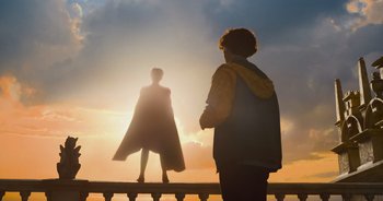 Movie still from “The Flash” (2023), directed by Andy Muschietti – A man standing on a ledge looking at a woman in a cape at sunset; Wide shot, Low angle