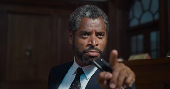 Movie still from “The Flash” (2023), directed by Andy Muschietti – A person wearing a suit and tie holding a pair of scissors; Close Up shot, Low angle