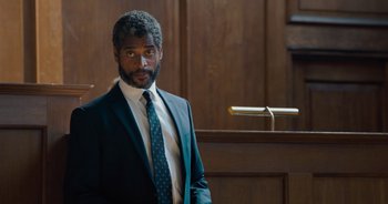 Movie still from “The Flash” (2023), directed by Andy Muschietti – A man in a suit and tie standing in front of a podium; Medium shot, Over the shoulder angle