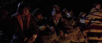Movie still from “The Fog” (1980), directed by John Carpenter – A group of people sitting on the ground next to a fire; Medium shot, Over the shoulder angle
