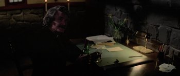Movie still from “The Fog” (1980), directed by John Carpenter – An older man sitting at a table with a glass of wine; Medium shot, High angle