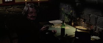 Movie still from “The Fog” (1980), directed by John Carpenter – An older man sitting at a table with a bottle of wine; Medium shot, High angle