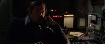 Movie still from “The Fog” (1980), directed by John Carpenter – A man sitting at a table in front of a microphone; Close Up shot, Over the shoulder angle