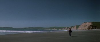 Movie still from “The Fog” (1980), directed by John Carpenter – A man walking on the beach with a surfboard; Extreme Wide shot, Low angle